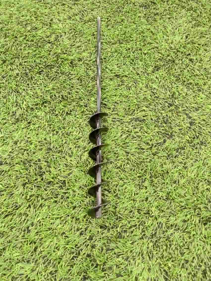 A steel SMART Base Auger designed for cleaning base anchors on a grassy surface.